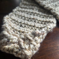 Chunky hand-knitted beige scarf with thick yarn on a wooden table