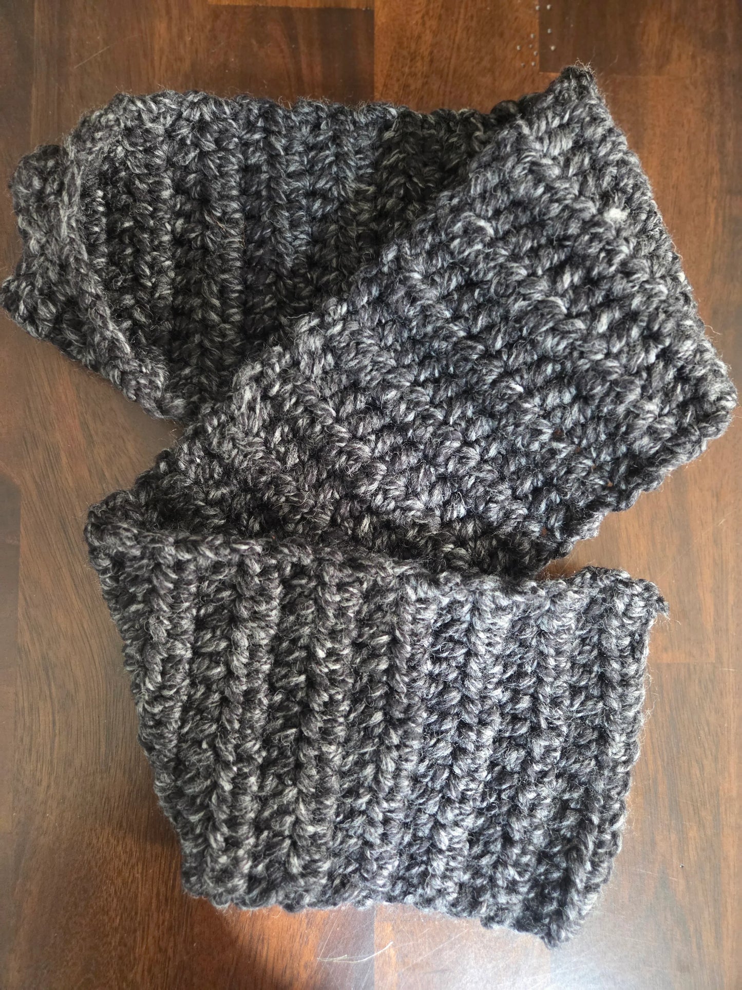 Handmade chunky dark gray crochet scarf on wooden surface