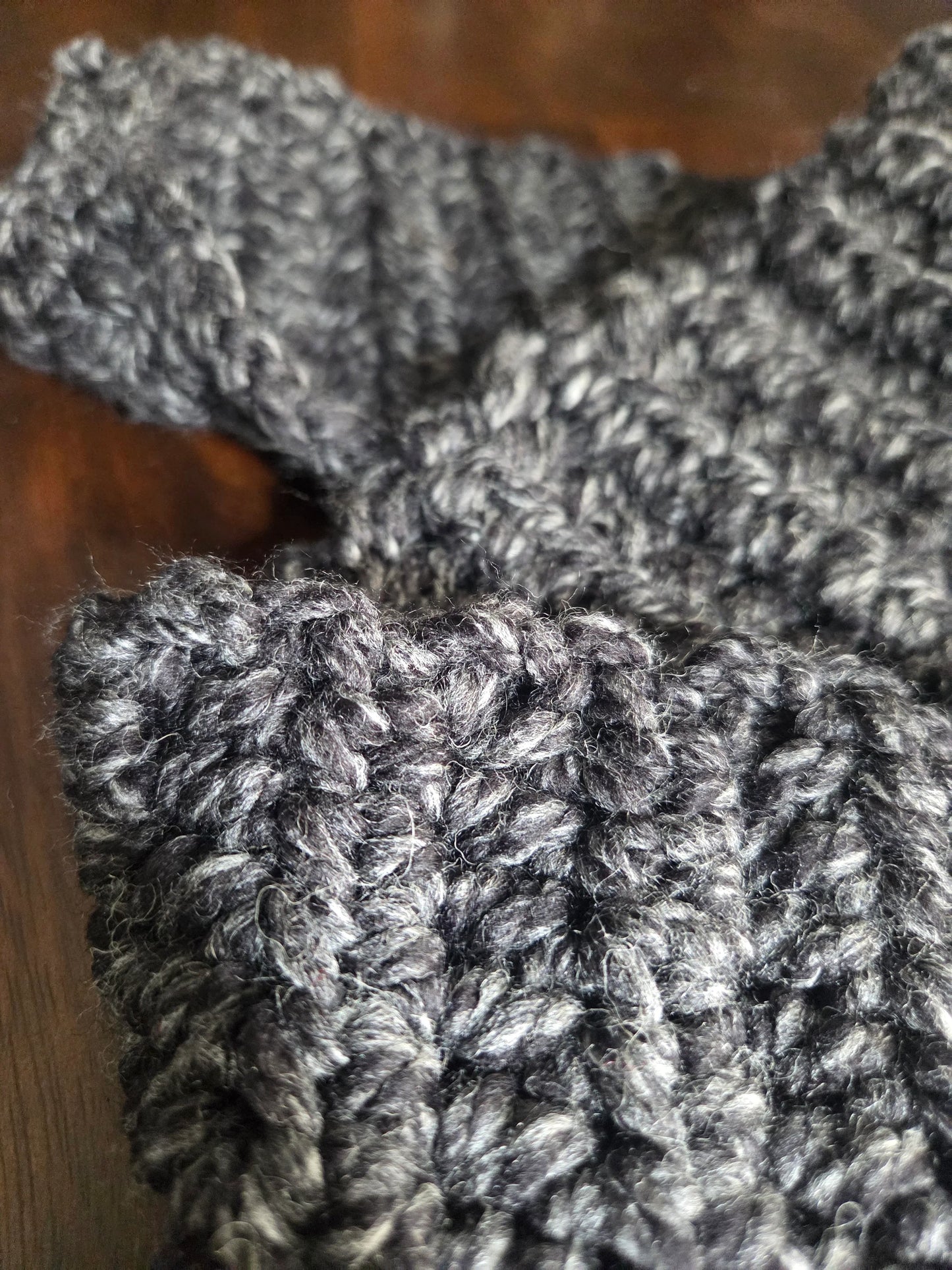Close-up of chunky dark gray knitted wool fabric on a wooden surface