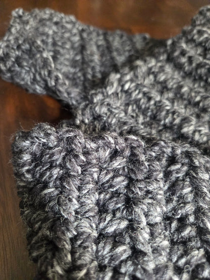 Close-up of chunky dark gray knitted wool fabric on a wooden surface