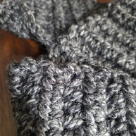 Close-up of chunky dark gray knitted wool fabric on a wooden surface