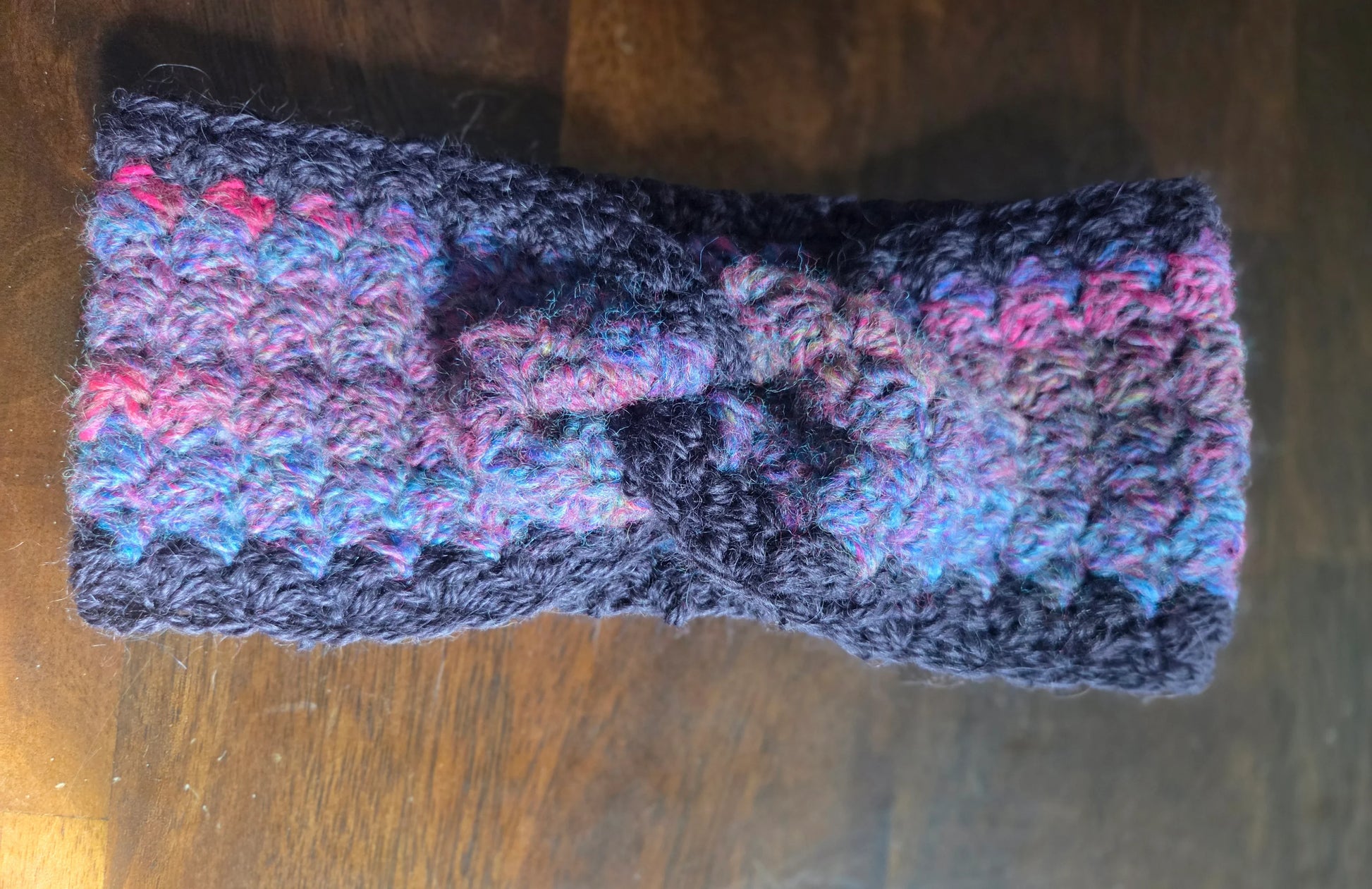 Handmade crochet ear warmer, multicolor yarn with knot, on wooden table