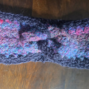 Handmade crochet ear warmer, multicolor yarn with knot, on wooden table