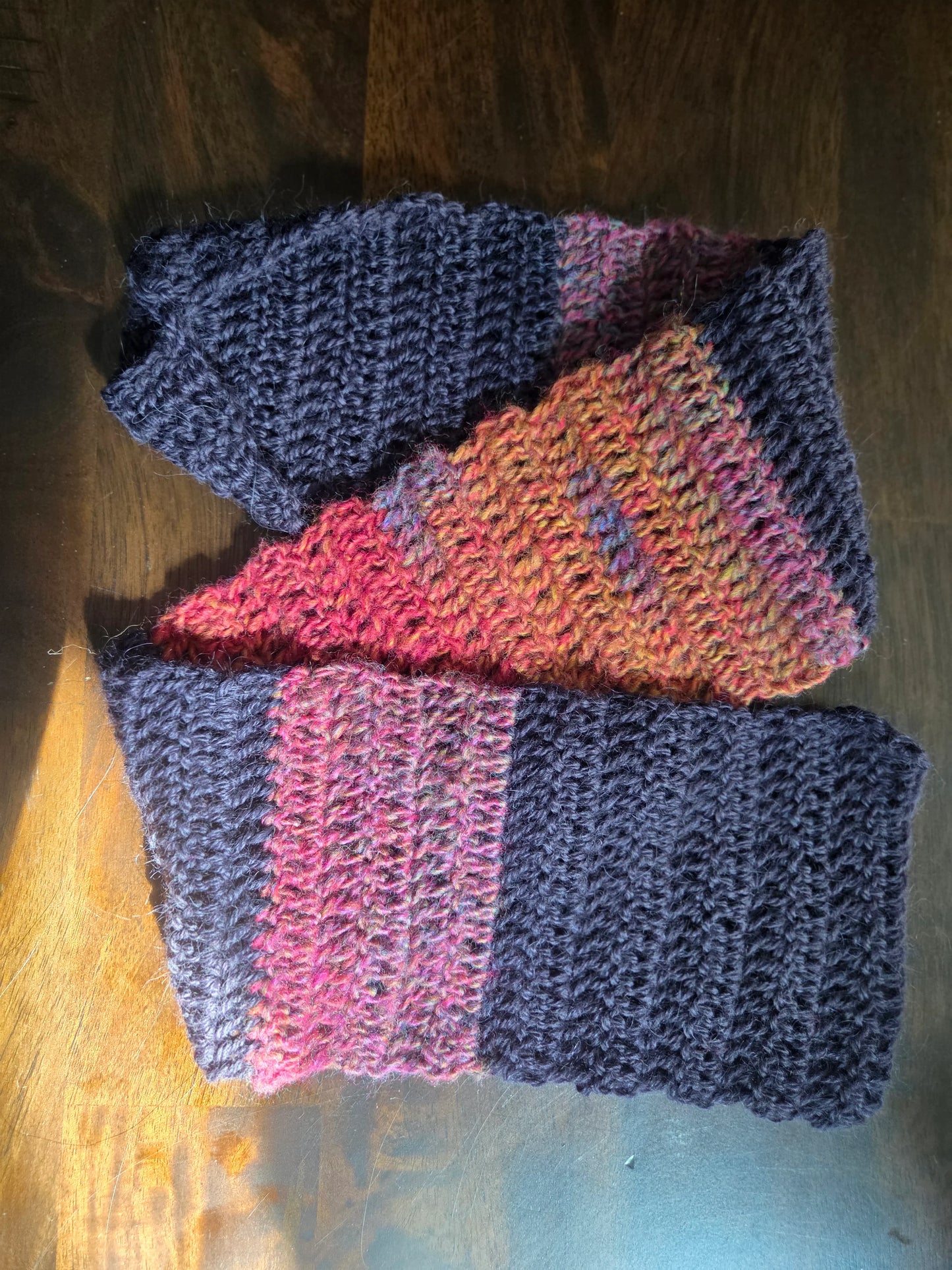 Handmade knitted scarf with navy and multicolor yarn on wooden surface