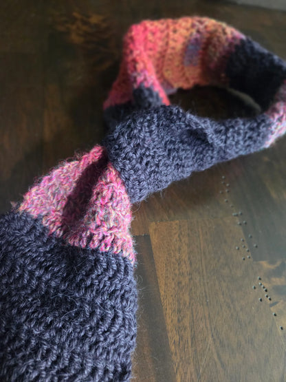 Handmade knit scarf with pink and dark gray stripes on wooden table