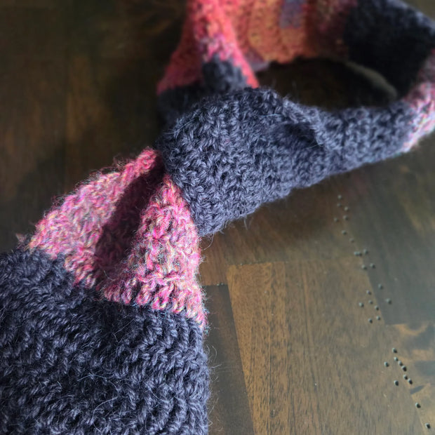 Handmade knit scarf with pink and dark gray stripes on wooden table