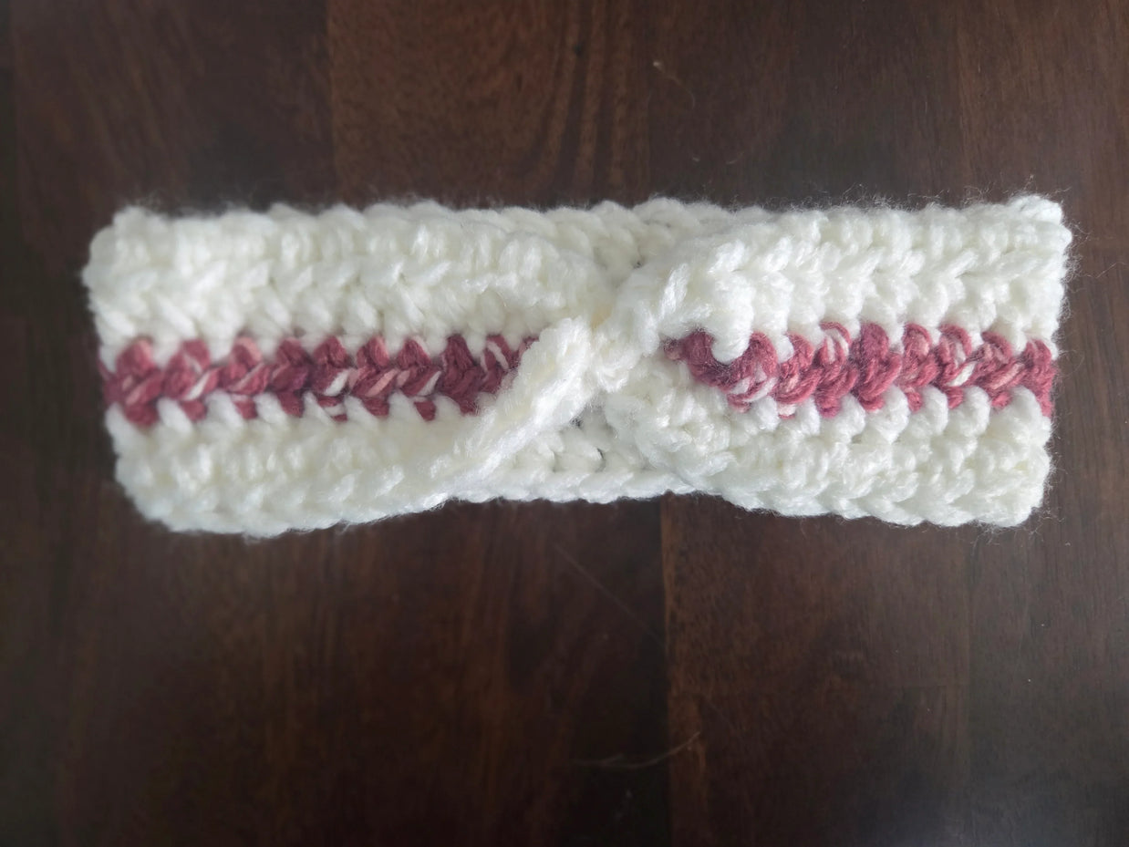 Handmade crochet headband with white yarn and pink accent on dark wooden table