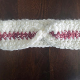 Handmade crochet headband with white yarn and pink accent on dark wooden table