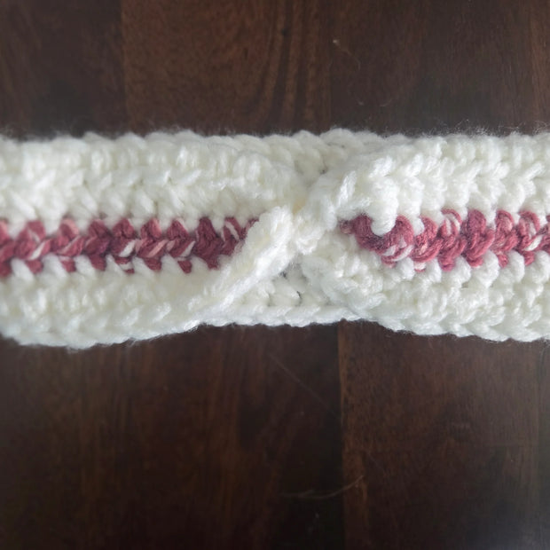 Handmade crochet headband with white yarn and pink accent on dark wooden table