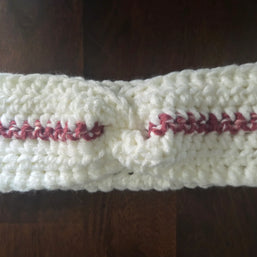 Handmade white crochet headband with pink stripe, knotted at center, on wooden table