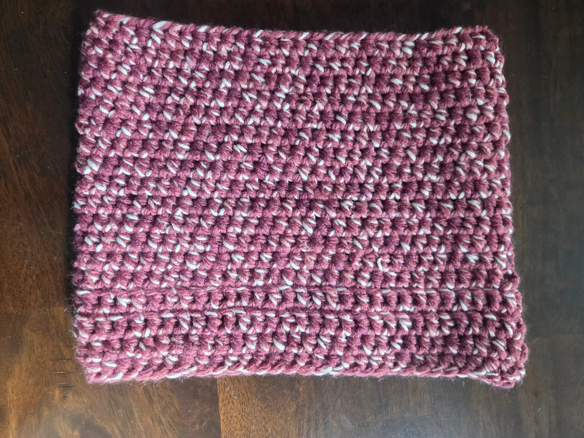 Handmade crochet cowl scarf in maroon and white yarn on wooden table
