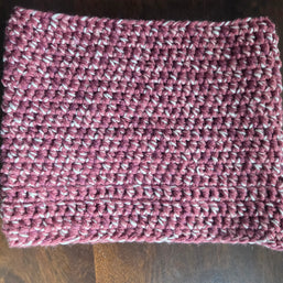 Handmade crochet cowl scarf in maroon and white yarn on wooden table