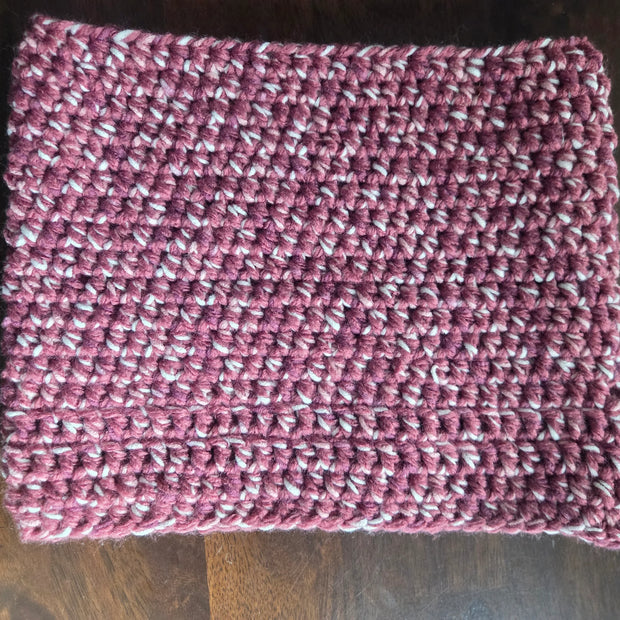 Handmade crochet cowl scarf in maroon and white yarn on wooden table
