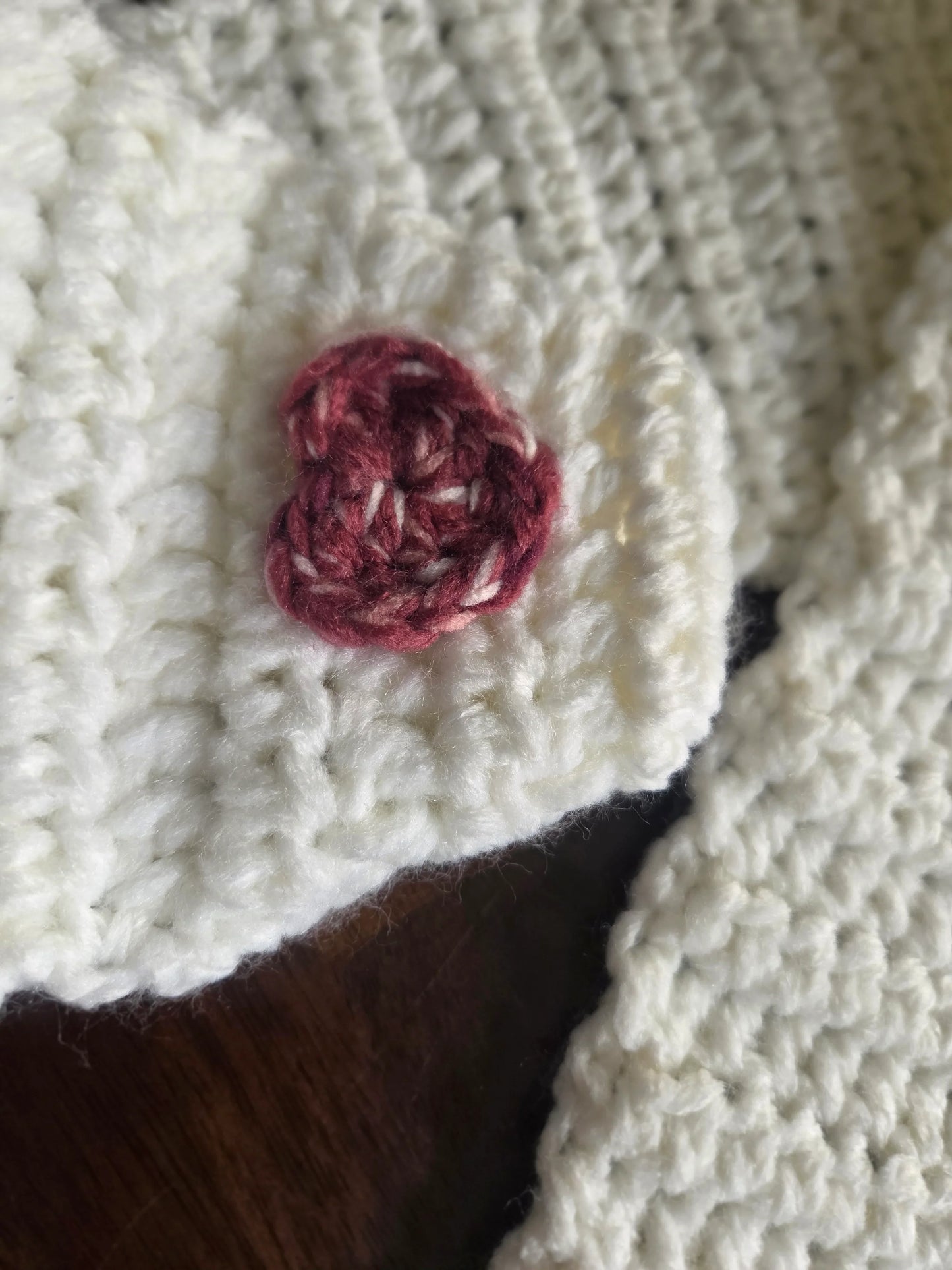 White crocheted fabric with red heart-shaped detail on dark wood surface