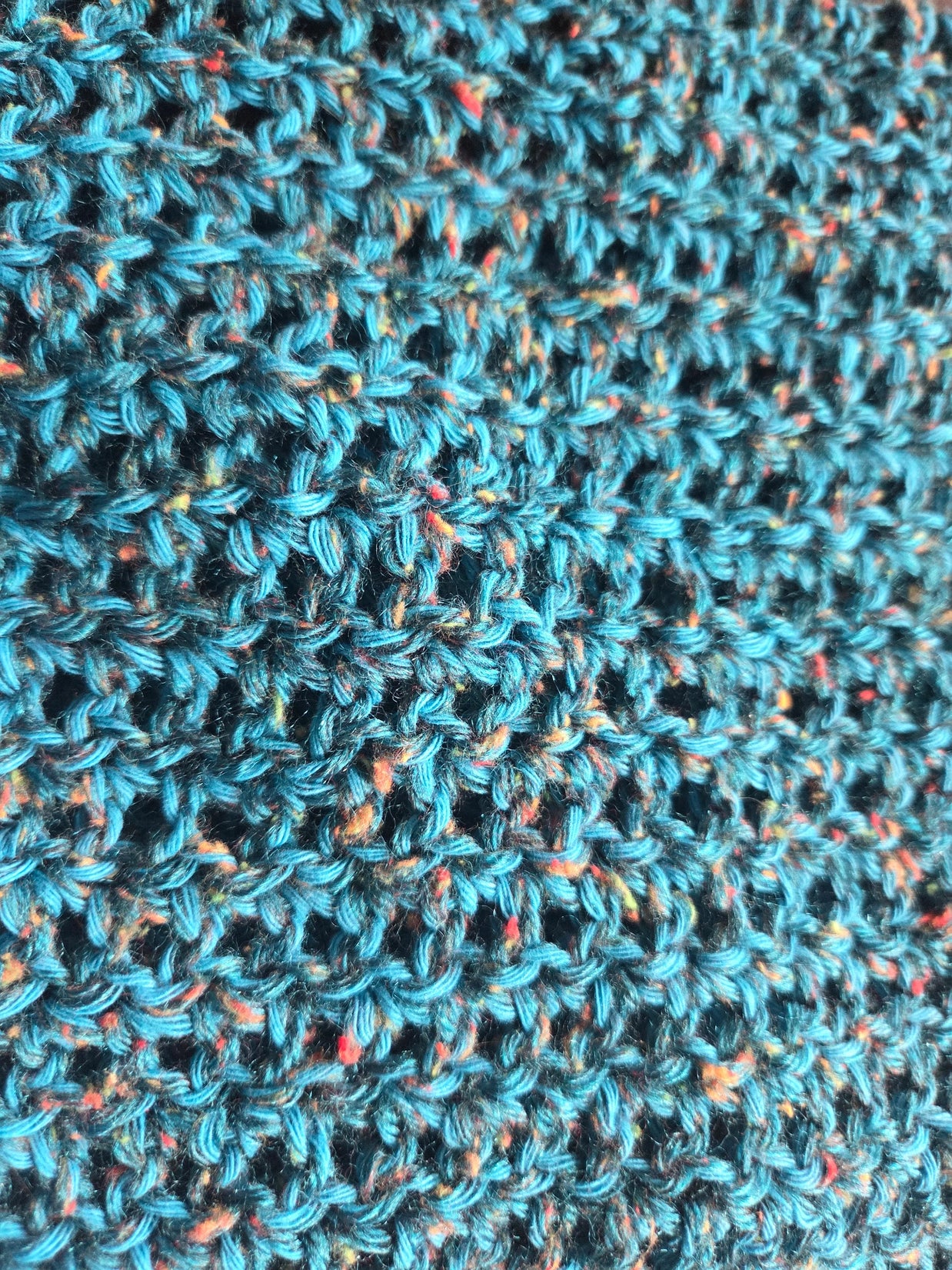Close-up of blue crochet fabric with colorful speckles and textured yarn pattern