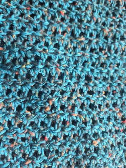 Close-up of blue crochet fabric with colorful speckles and textured yarn pattern