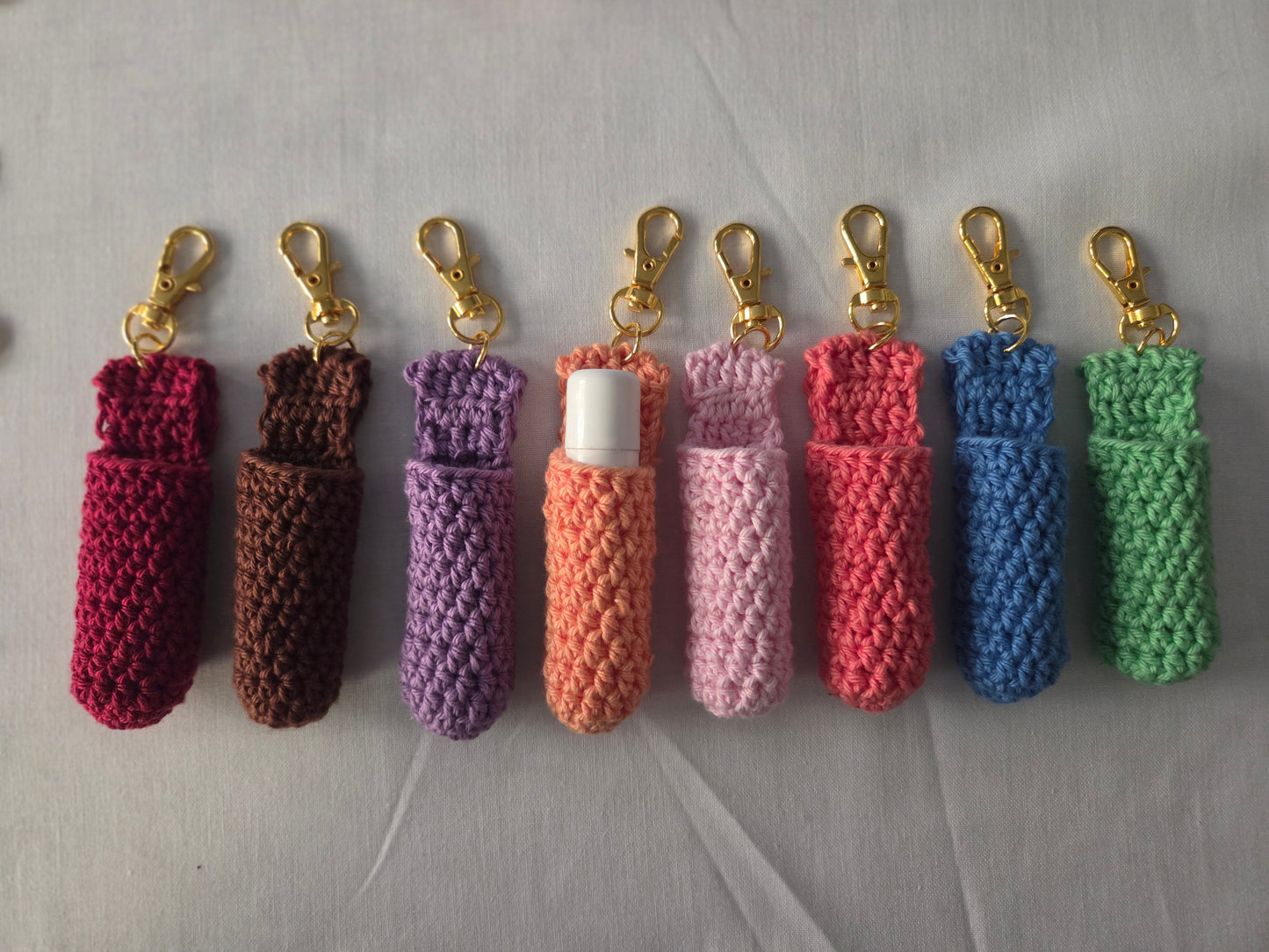 Colorful crochet lip balm holders with gold keychains on light background