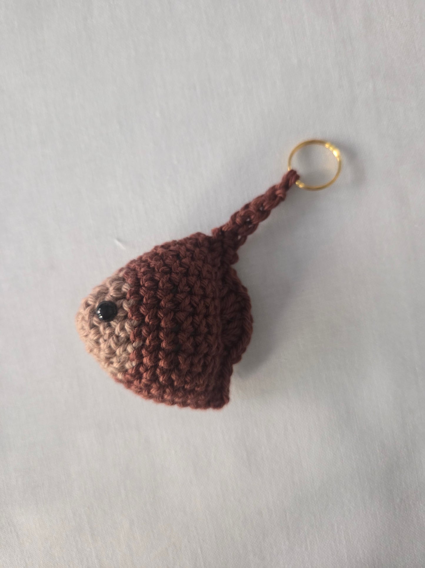 Handmade brown crochet keychain with black bead eye on a plain light background