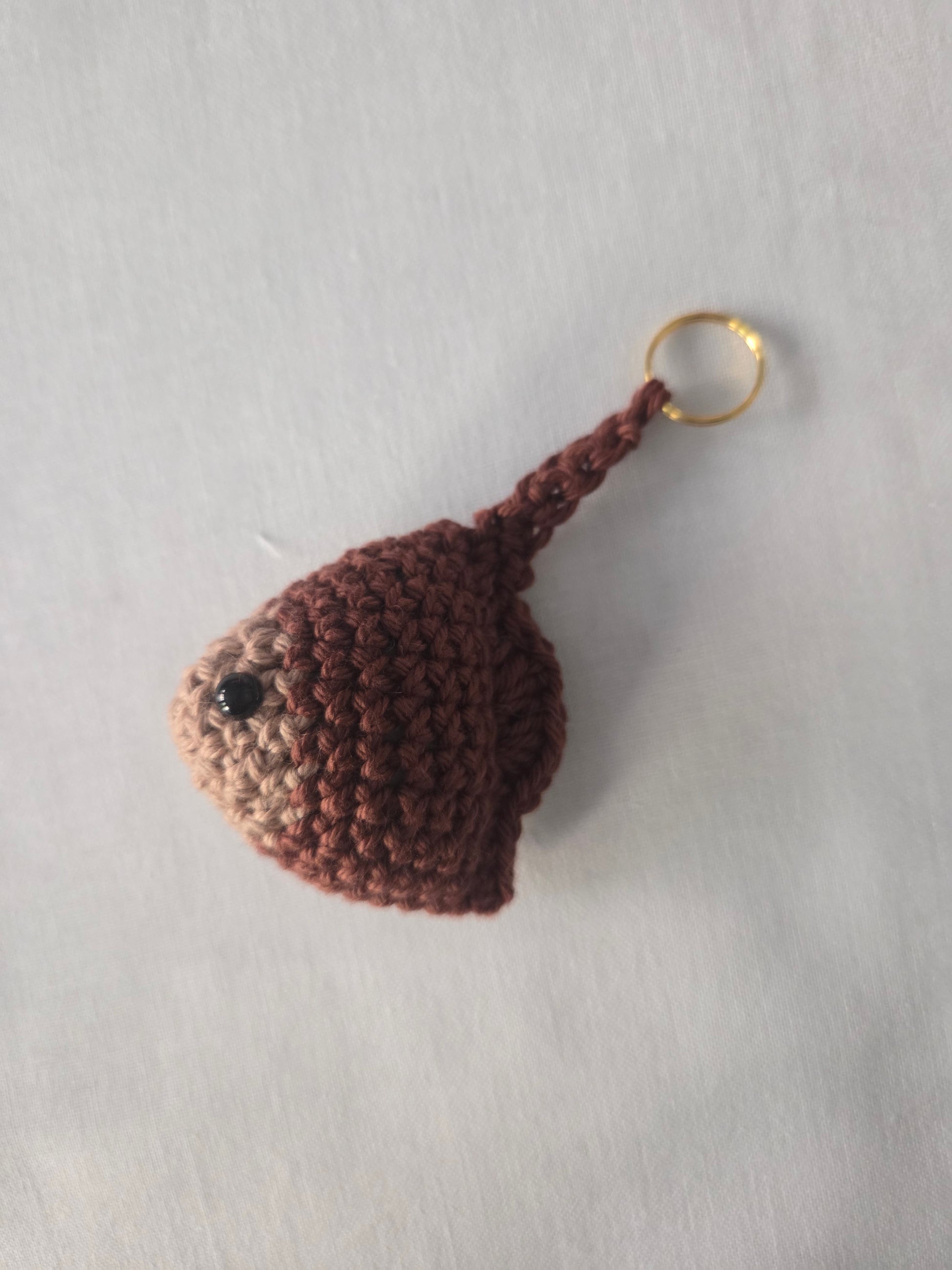 Handmade brown crochet keychain with black bead eye on a plain light background