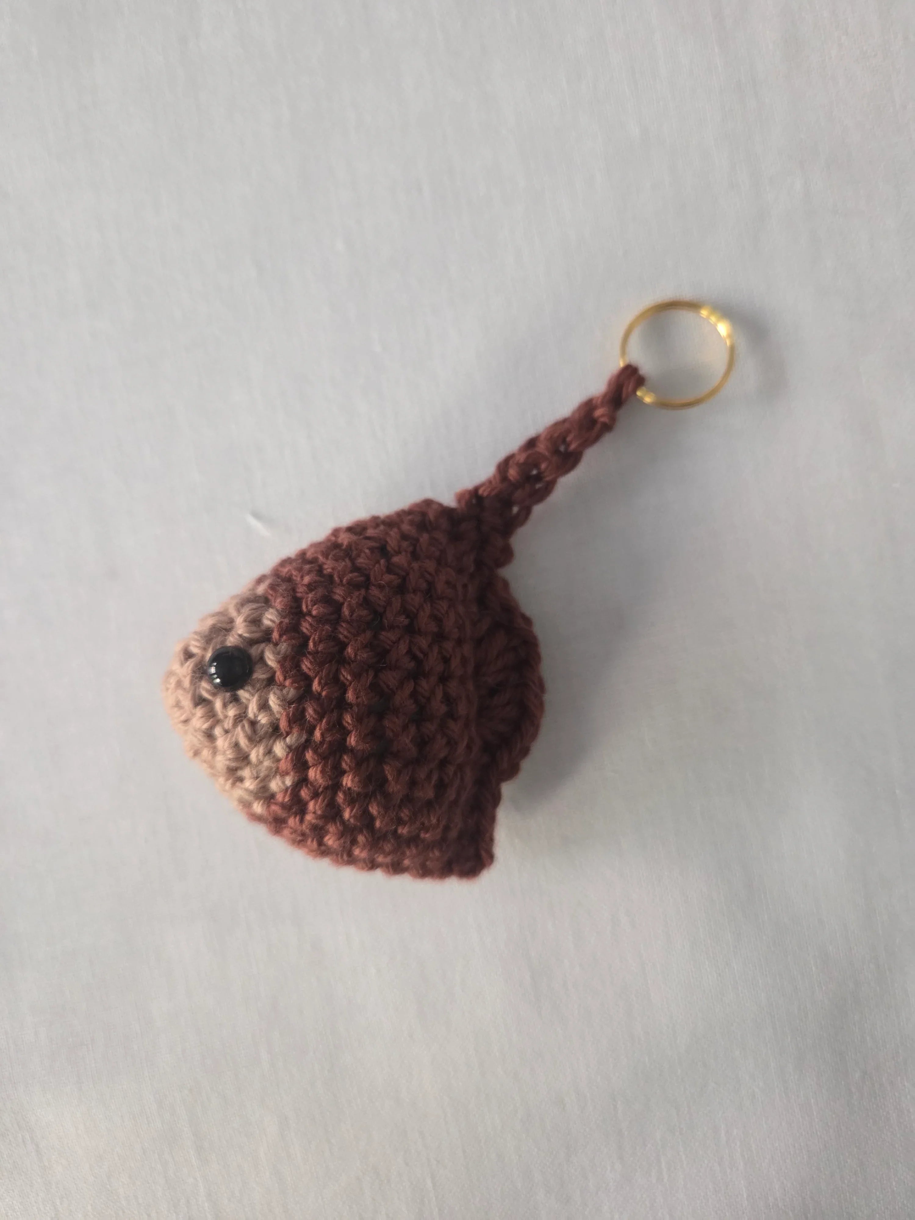 Handmade brown crochet keychain with black bead eye on a plain light background