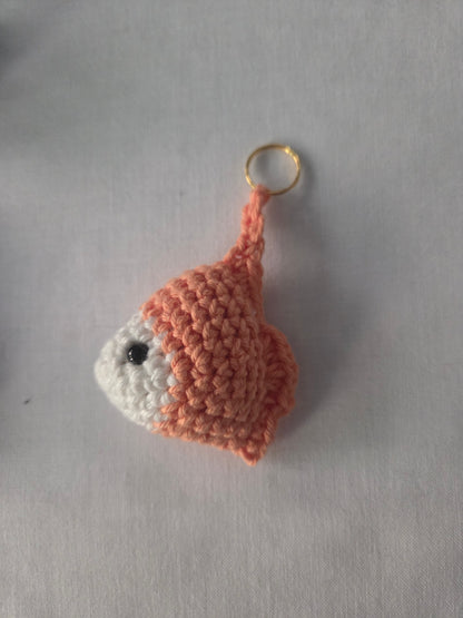 Handmade crochet goldfish keychain with orange and white yarn on a white background.