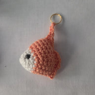Handmade crochet goldfish keychain with orange and white yarn on a white background.