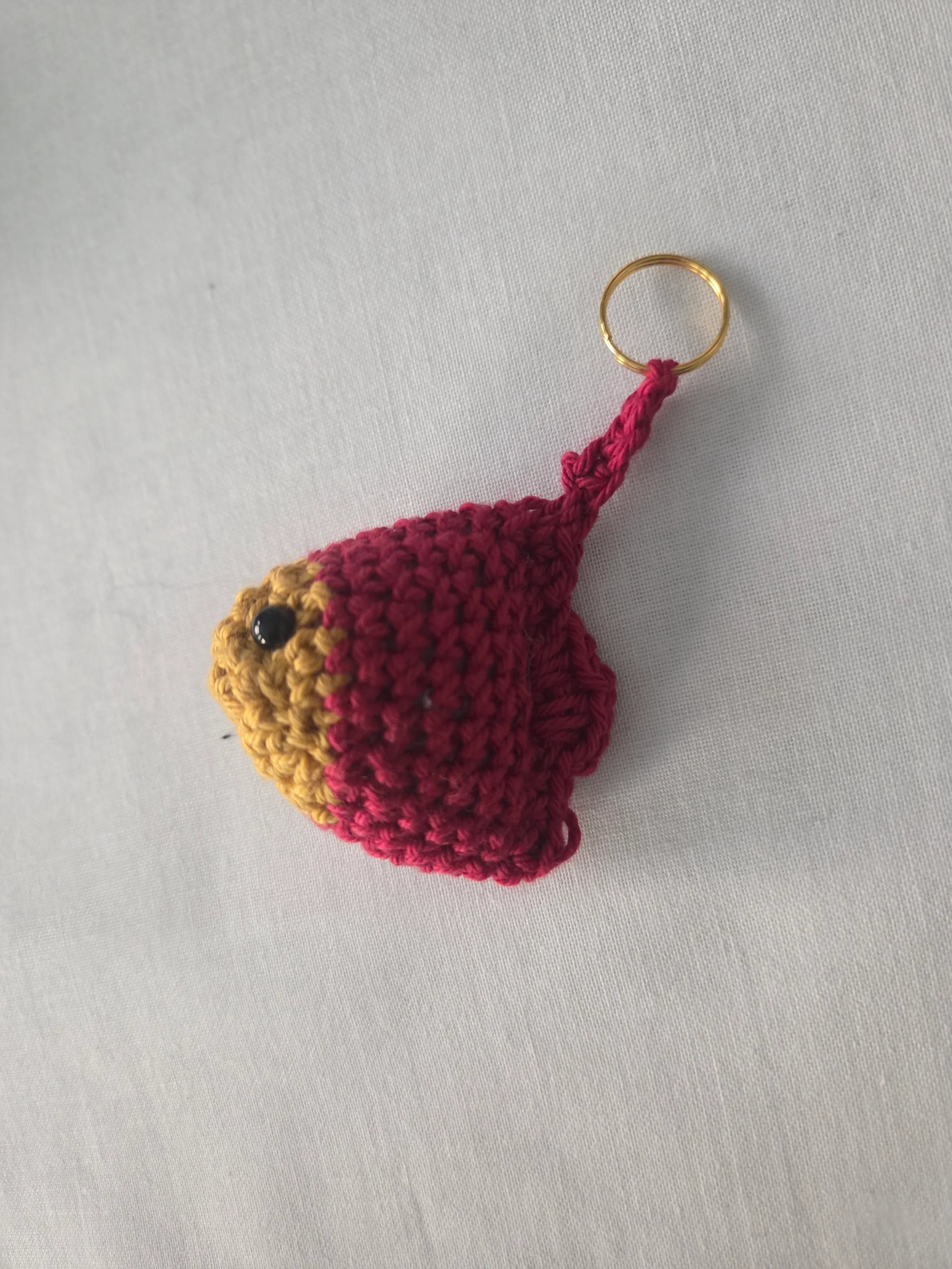 Handmade crochet fish keychain in red and yellow yarn on white fabric background