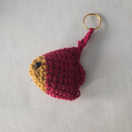 Handmade crochet fish keychain in red and yellow yarn on white fabric background