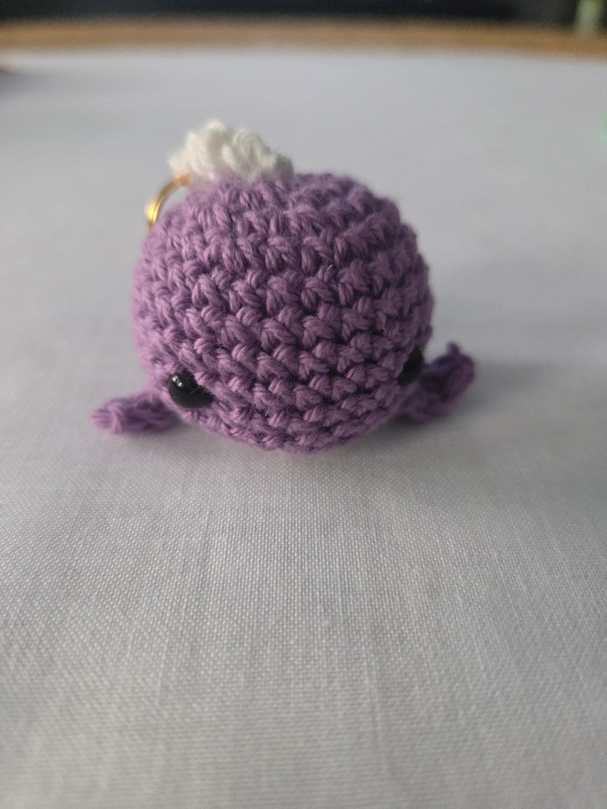Purple crochet amigurumi plush keychain with black eyes on a white surface
