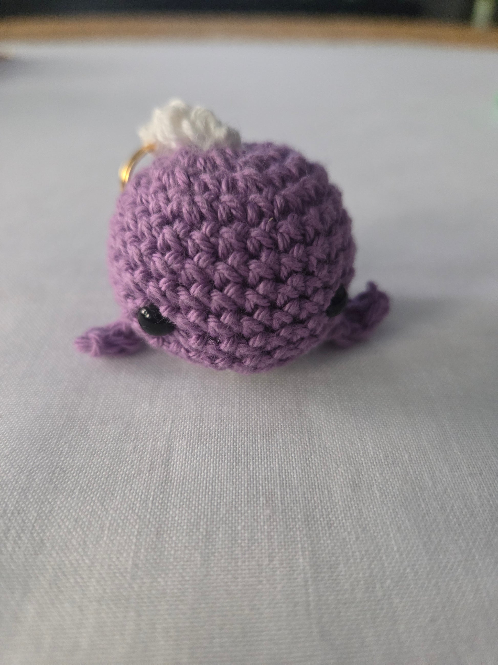 Purple crochet amigurumi plush keychain with black eyes on a white surface