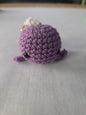 Purple crochet amigurumi plush keychain with black eyes on a white surface