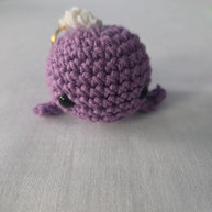 Purple crochet amigurumi plush keychain with black eyes on a white surface