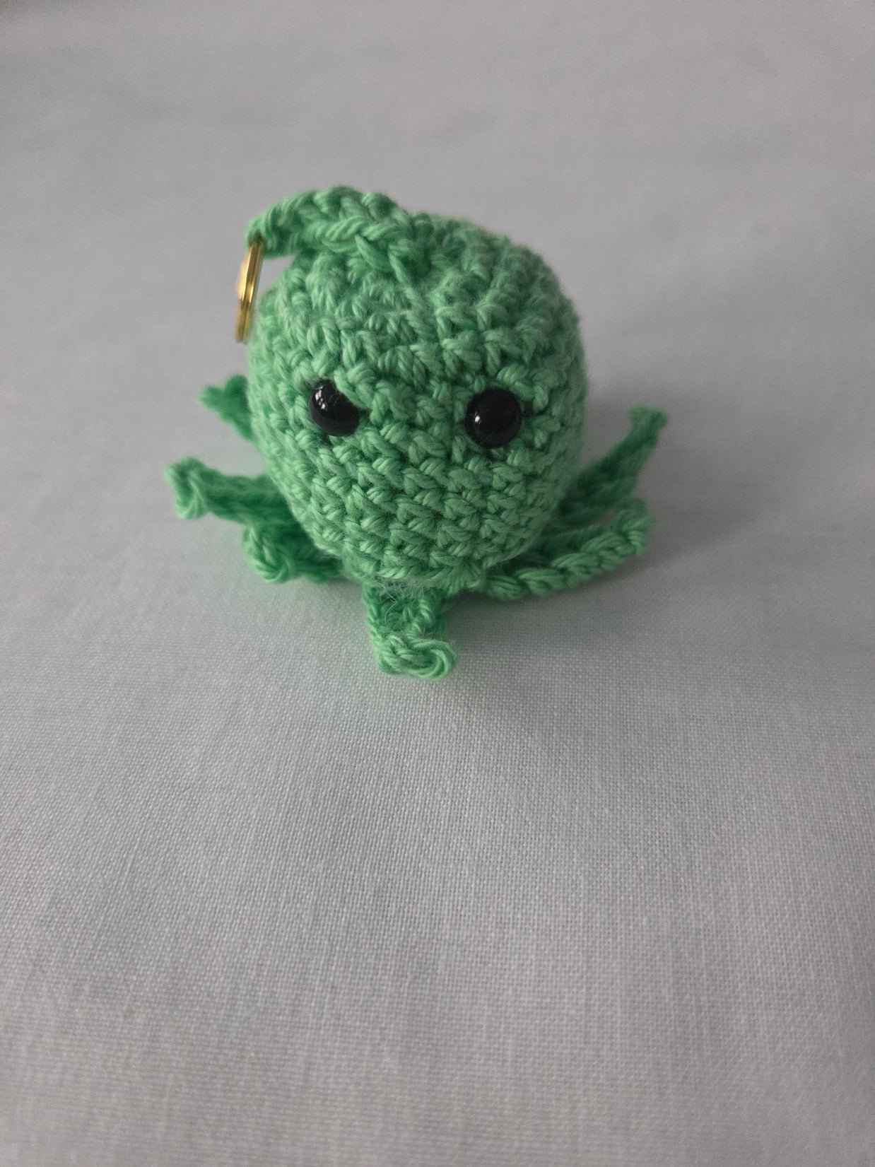 Handmade green crochet octopus keychain with black eyes on a light fabric background