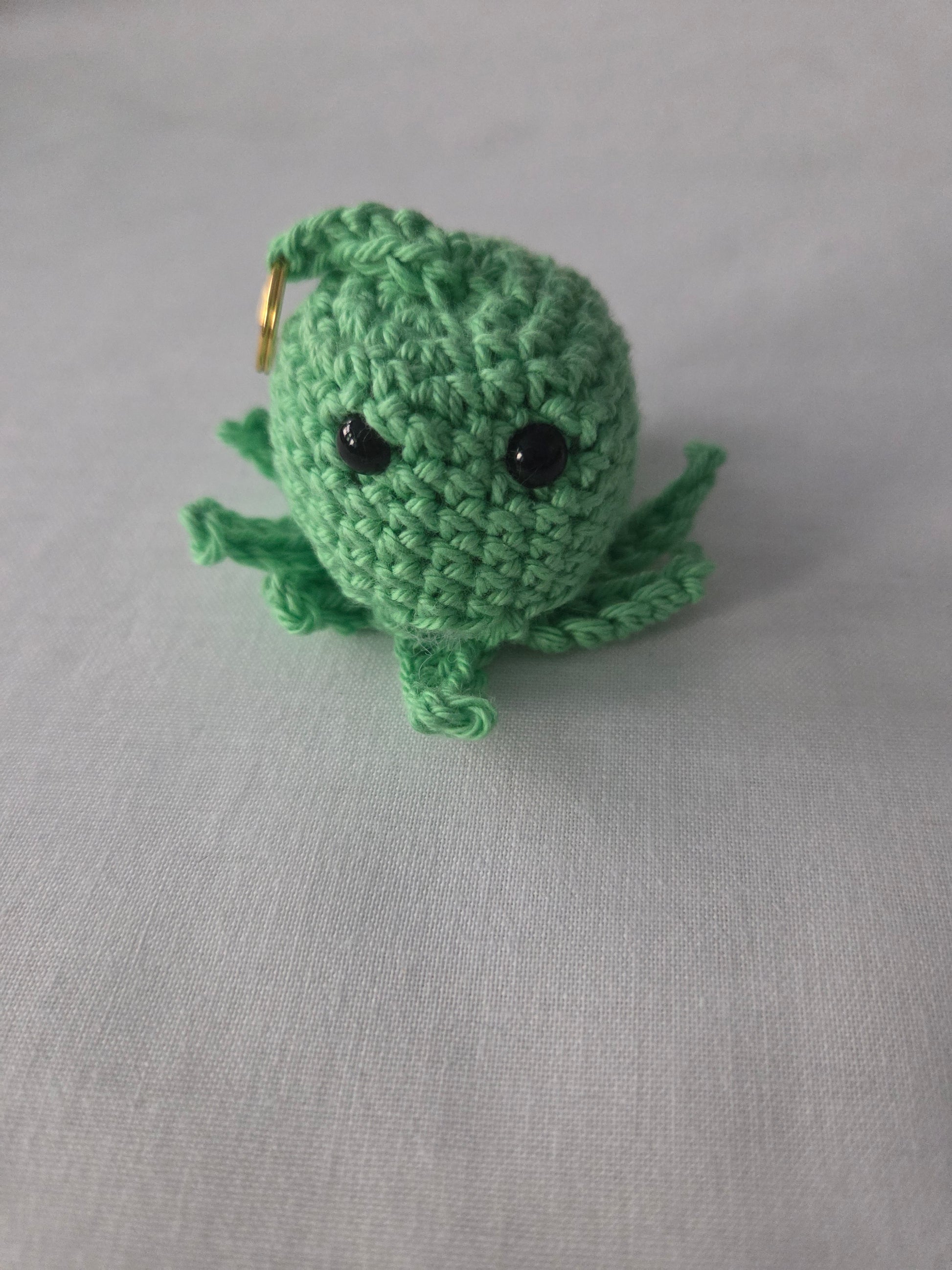 Handmade green crochet octopus keychain with black eyes on a light fabric background