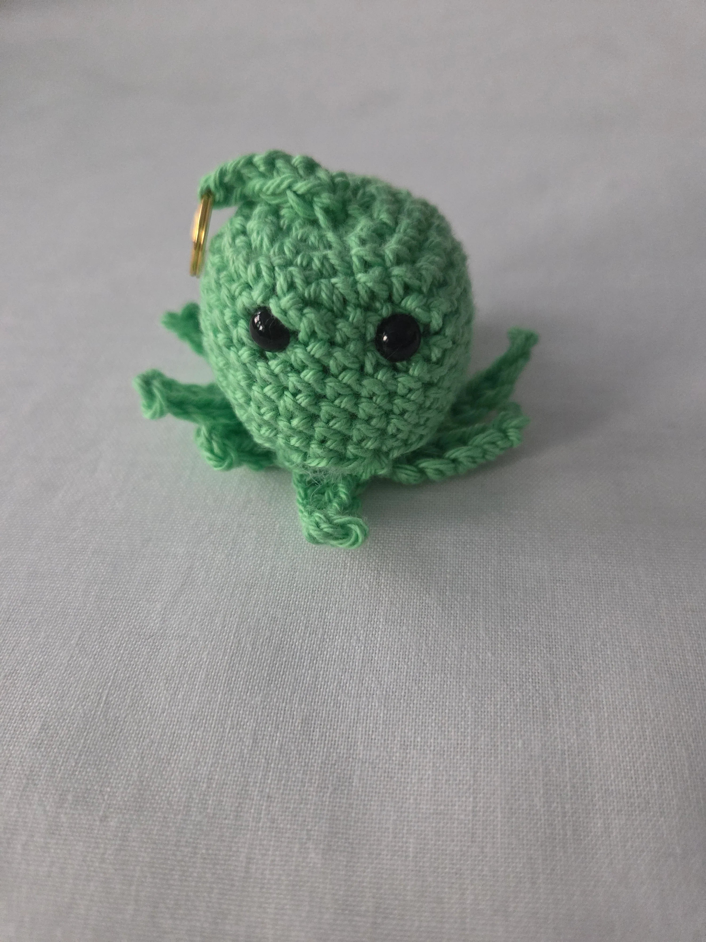 Handmade green crochet octopus keychain with black eyes on a light fabric background
