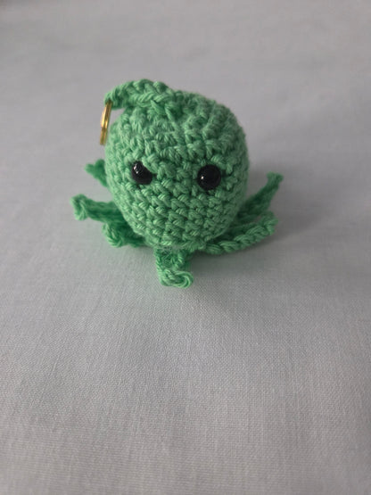 Handmade green crochet octopus keychain with black eyes on a light fabric background