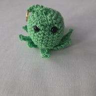 Handmade green crochet octopus keychain with black eyes on a light fabric background