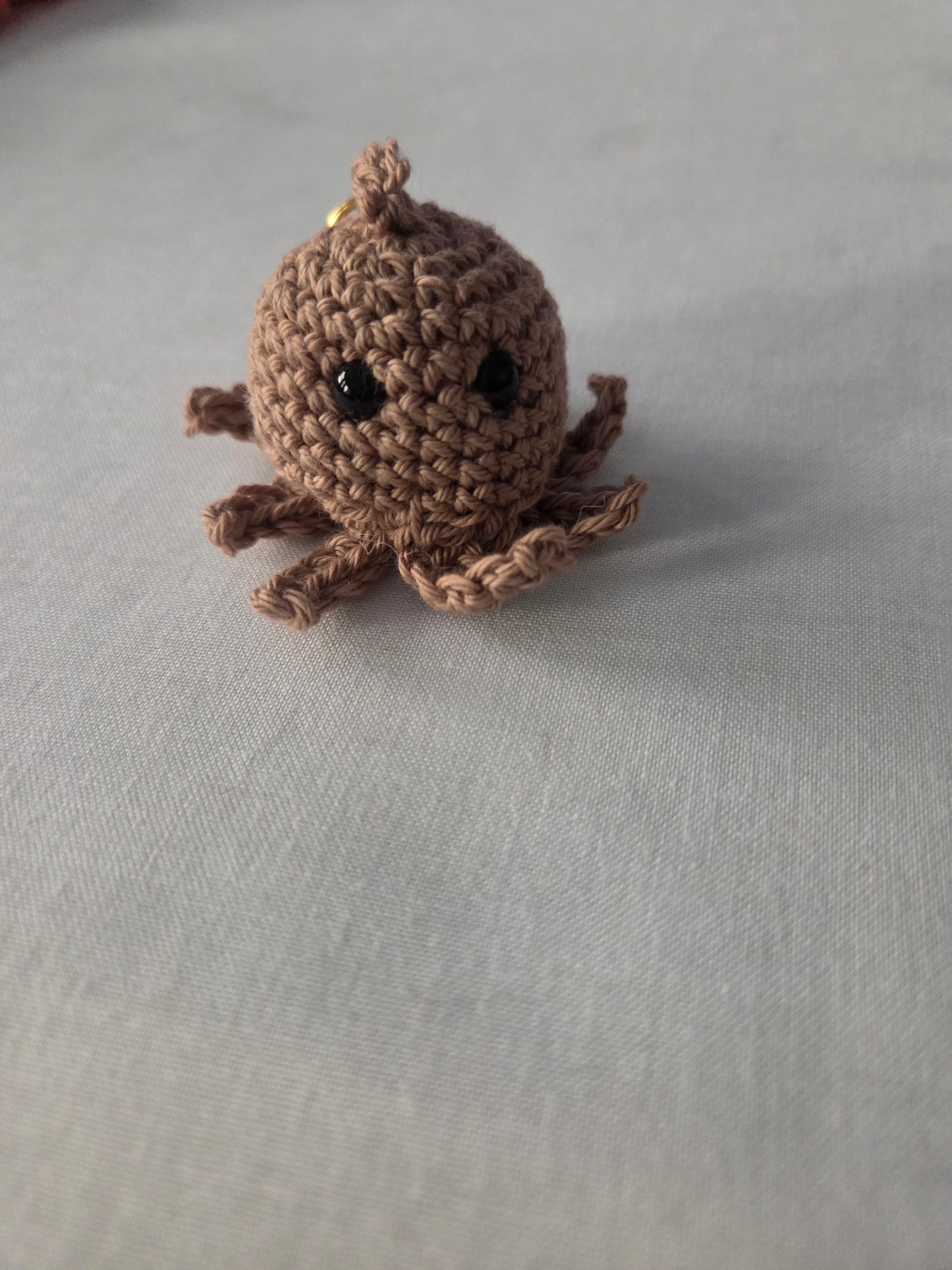 Handmade brown crochet octopus plush keychain on a light fabric background