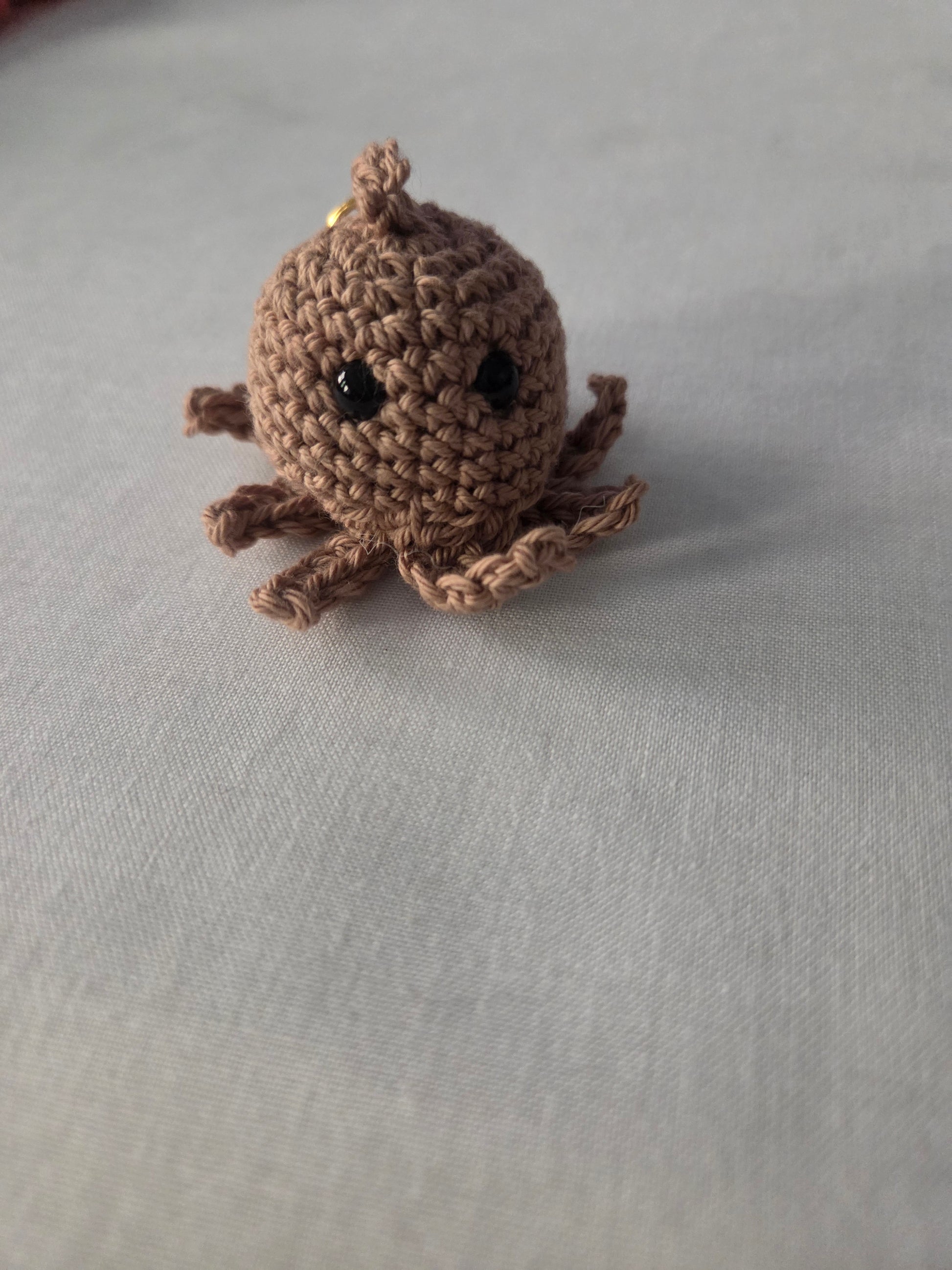 Handmade brown crochet octopus plush keychain on a light fabric background