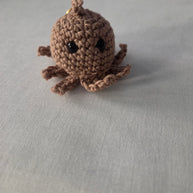 Handmade brown crochet octopus plush keychain on a light fabric background