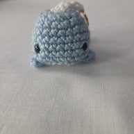 Handmade blue crochet whale keychain on white fabric background