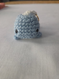 Handmade blue crochet whale keychain on white fabric background