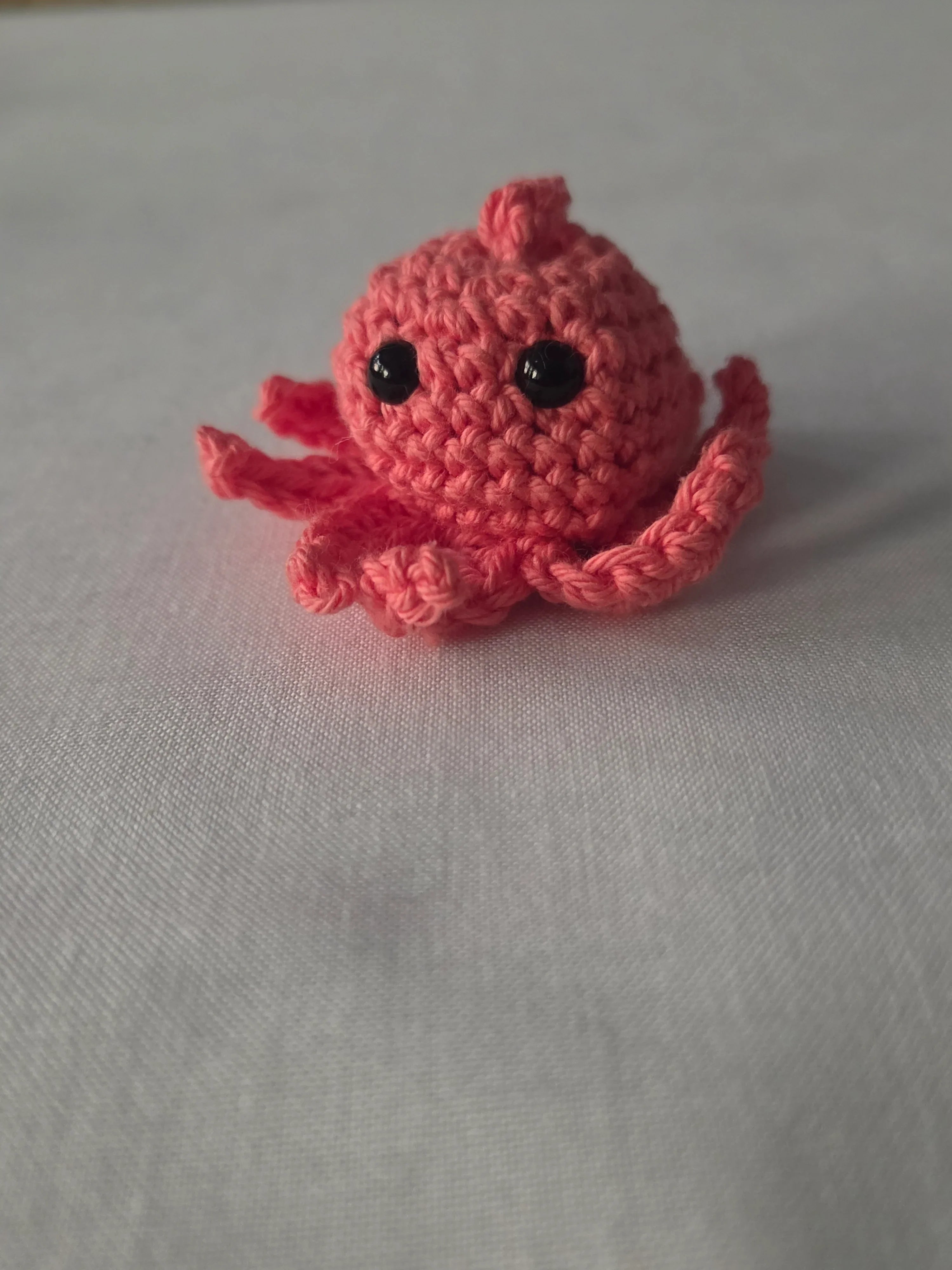 Pink crocheted octopus amigurumi toy with black eyes on a white surface