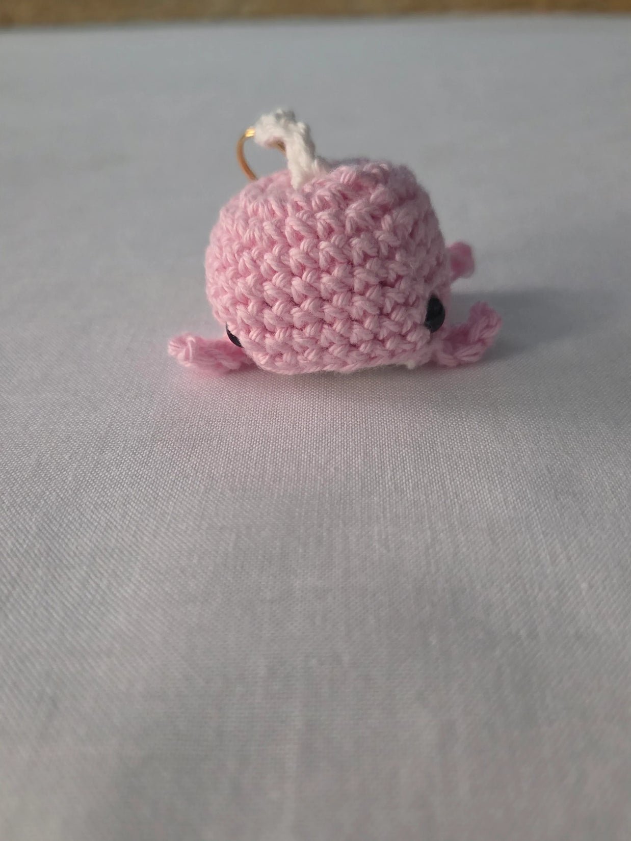 Pink crocheted whale keychain on white fabric background