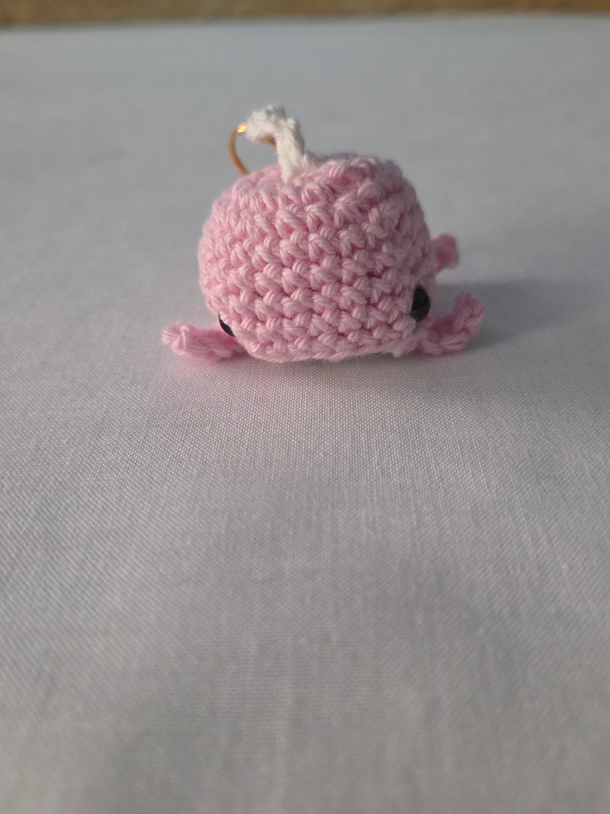 Pink crocheted whale keychain on white fabric background