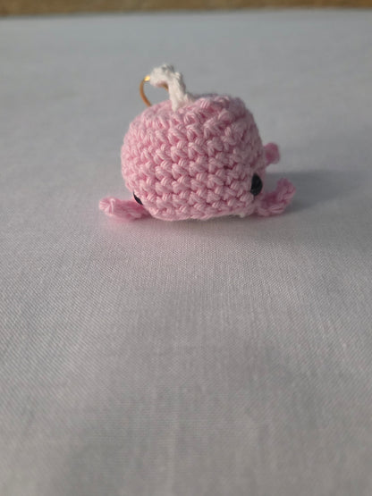 Pink crocheted whale keychain on white fabric background