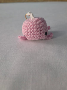 Pink crocheted whale keychain on white fabric background