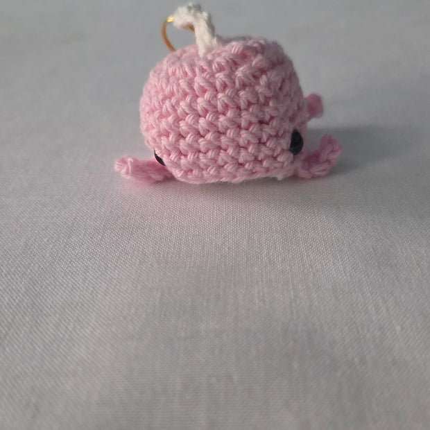 Pink crocheted whale keychain on white fabric background
