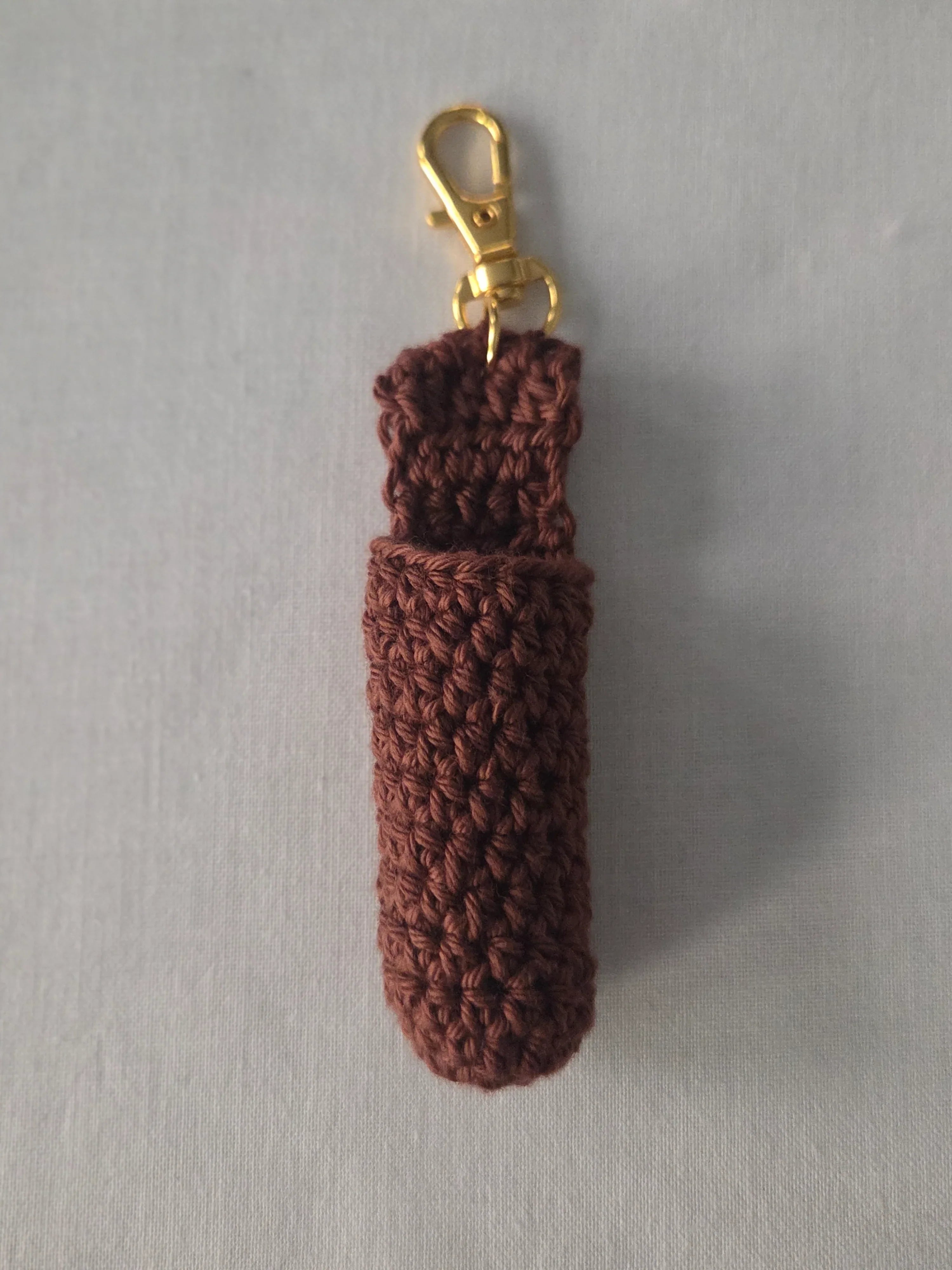 Brown crochet keychain pouch with gold clasp on light gray background