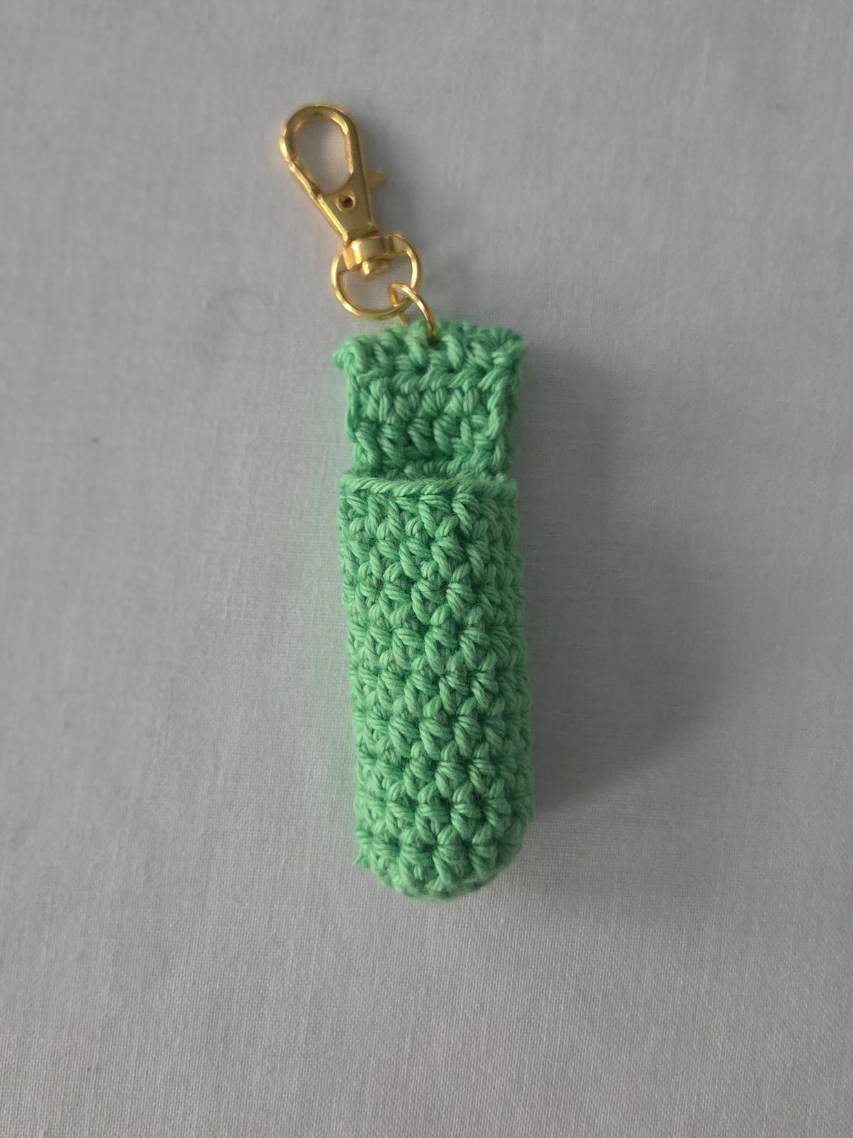 Green crocheted keychain with a gold clasp on a gray background